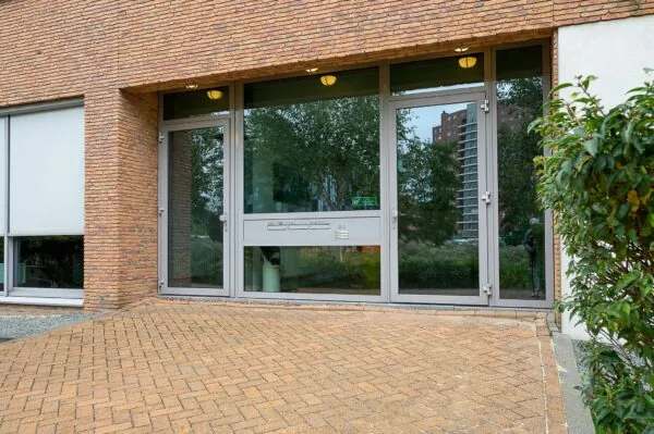 Ingang van een modern appartementencomplex aan de Jacques Dutilhweg met grote glazen deuren en brievenbussen.